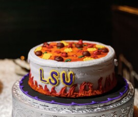 A pizza-themed LSU cake with flames sits on a silver stand over a white tablecloth—fun New Orleans wedding idea.