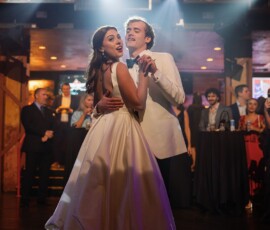 Bride and groom in white dance joyfully under stage lights at a charming Gulf South wedding, guests watching in the background.