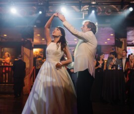Bride and groom dance under dramatic lighting at their New Orleans wedding, guests watching from floor and balcony above.