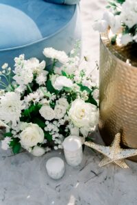 White roses, greenery, candles, and a gold vase on sand with a starfish—elegant Gulf South Louisiana wedding inspiration.