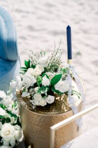 Elegant Louisiana wedding scene: gold table on sand with white bouquet, blue candle, and light blue chair.
