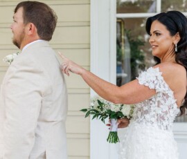 Bride in white gown taps groom’s shoulder from behind, bouquet in hand, at a beautiful Louisiana wedding.