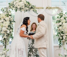 Bride and groom smile under a white floral arch with an officiant—New Orleans wedding ceremony inspiration.