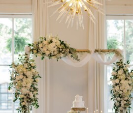 Elegant Gulf South wedding with white flowers, candles, gold accents, cake, and spiked chandelier in a sunlit room.
