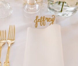 Elegant white place card with “Jeffrey” in gold script, gold cutlery, and glassware on a white New Orleans wedding table.