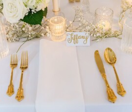 Elegant table with gold utensils, white napkin, candles, white flowers, and place card—sophisticated New Orleans wedding decor.