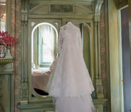White lace wedding dress on a mirror in a vintage room with green woodwork and floral wallpaper, New Orleans elegance.