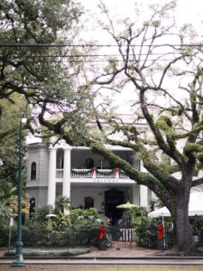 White house with columns, holiday decor, red bows on railings, trees in front; known as Columns, a popular Louisiana wedding venue.