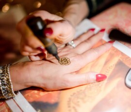 Henna is applied in a floral design on manicured, red-painted hands with jewelry, capturing Gulf South wedding elegance.
