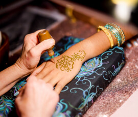 Henna artist with bangles decorates a hand on a colorful cushion at an Indian wedding in New Orleans.