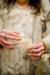 A person in a beaded outfit holds a cone cup and white sweet, showing gold nails and silver rings at a New Orleans wedding.