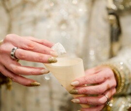 A person in a beaded outfit holds a cone cup and white sweet, showing gold nails and silver rings at a New Orleans wedding.