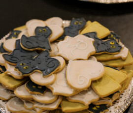 Decorated cookies shaped like black cats, ghosts, and tombstones on a silver tray with lace doily—festive New Orleans treat.