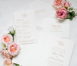 Gold script wedding invitations and envelopes on white, with blush pink and cream flowers for a New Orleans or Indian wedding.