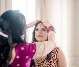 Woman in maroon and gold helps another adjust her headpiece for an Indian wedding at The Ritz-Carlton New Orleans.