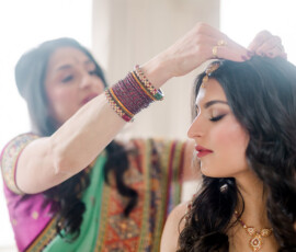 Two women in vibrant sarees prepare for an Indian wedding in New Orleans, sharing a quiet, elegant moment.