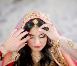 South Asian bride in red veil with jeweled headpiece adjusted, eyes closed at Ritz-Carlton New Orleans wedding.