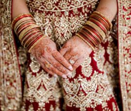 Woman in red and gold sari with henna and bangles, hands clasped, at elegant Ritz-Carlton New Orleans wedding.