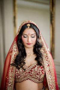 Woman in red and gold embroidered outfit with veil, jewelry, and wavy dark hair—ideal Louisiana wedding inspiration.