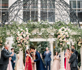 Bride and groom kiss under a flowered gazebo at an elegant multicultural Indian wedding in New Orleans.