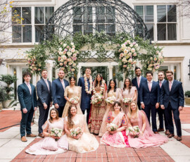 Indian wedding party under floral arch at The Ritz-Carlton New Orleans, joyful bride, groom, bridesmaids, and groomsmen smiling.