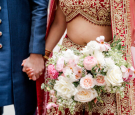 Couple holding hands at their New Orleans Indian wedding; she wears a red lehenga, he’s in a blue traditional outfit.