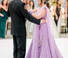 A couple dances at a Gulf South wedding; she wears a lavender gown, he’s in a black suit, as guests watch elegantly.
