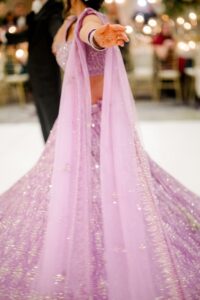 Woman in a sparkly lavender outfit dances with outstretched arm at a lively New Orleans wedding; blurred guests and lights behind.