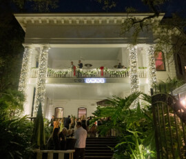 The Columns Hotel lit by string lights, with people celebrating outside and lush greenery at night.
