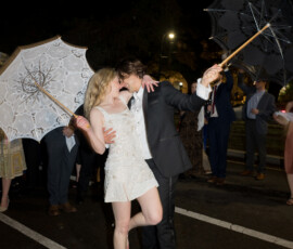 A formally dressed couple kisses at night in the street with umbrellas, celebrating a New Orleans second line wedding.