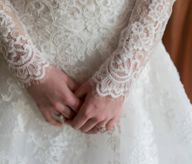 Bride in a white lace long-sleeve wedding dress clasps hands at waist, exuding timeless Holy Name of Jesus New Orleans elegance.