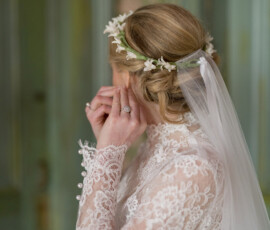 Bride in lace dress and floral veil adjusts earring, facing away, before Holy Name of Jesus New Orleans wedding.