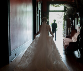 Bride in lace gown walks a dim hallway toward a sunlit doorway at The Columns Hotel, New Orleans wedding.