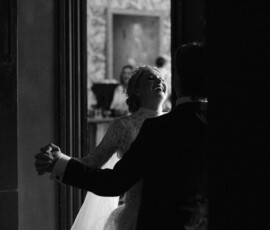 Bride and groom dance at The Columns Hotel in New Orleans, smiling as guests and patterned wallpaper fill the charming venue.