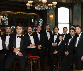 A group of men and a boy in tuxedos pose in a vintage bar at The Columns Hotel New Orleans wedding.