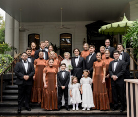 Wedding party on steps of The Columns Hotel New Orleans, with couple, bridesmaids in copper, groomsmen, and children in white.