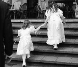 Two girls in white dresses hold hands on stone steps at a New Orleans wedding, black and white photo, outdoor setting.