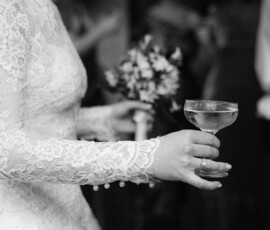 Bride in lace dress with bouquet and champagne, joyful at Holy Name of Jesus New Orleans wedding. Black and white photo.