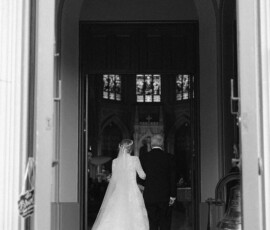 Bride and groom, backs to camera, enter Holy Name of Jesus New Orleans church hand in hand before their wedding.