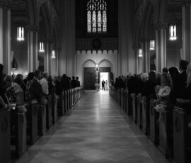 Black and white photo of a New Orleans wedding at The Columns Hotel, bride walks aisle as light streams through stained glass.