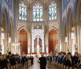 Bride in white gown walks down aisle with older man at Holy Name of Jesus New Orleans, ornate church filled with guests.