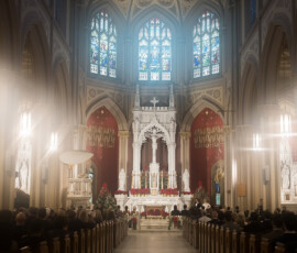 Congregation in pews faces ornate altar with white statues, red decor, stained glass, and sunlight at Holy Name of Jesus New Orleans.