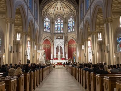 A congregation sits in pews facing an ornate church altar with red and gold decor and stained glass windows—Gulf South wedding inspiration.