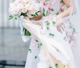 Bride in floral-embroidered dress holding pale pink and white rose bouquet outdoors, perfect for Gulf South wedding inspiration.