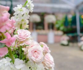 Floral arrangement with pink roses, white hydrangeas, and greenery; blurred garden or wedding setting in the background.