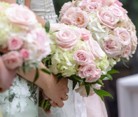 Guests in light floral dresses hold pink rose and white hydrangea bouquets at a formal Gulf South wedding or reception.
