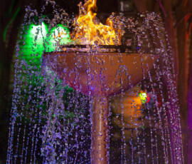 Fountain with water jets and a vibrant flame, lit by colorful lights at night—elegant New Orleans wedding inspiration.