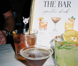 Three cocktails on a marble bar, with unique garnishes, in front of The Bar Signature Drinks sign at a chic New Orleans wedding.
