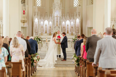 Bride and groom hold hands at a church altar, with guests watching a classic Louisiana wedding ceremony.