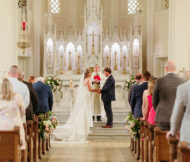 Bride and groom hold hands at a church altar, with guests watching a classic Louisiana wedding ceremony.